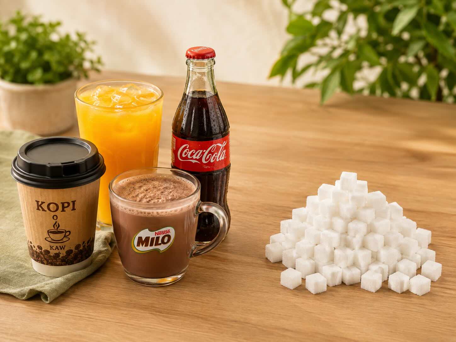 kopi, Milo, orange juice and Coke beside a glass jar of sugar, illustrating how sugar affects cholesterol